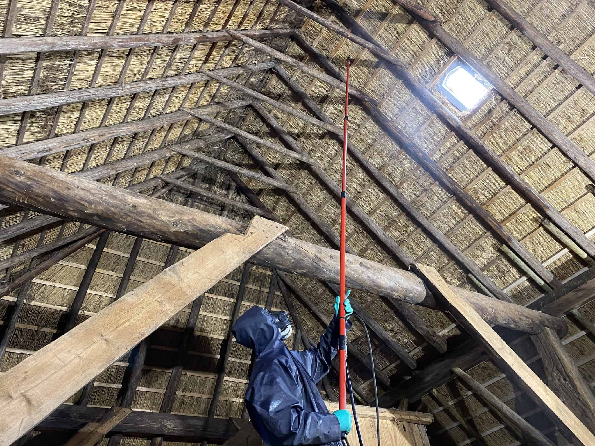 Persoon in beschermende kleding behandelt houten balken van een dakconstructie met verduurzamingsmiddel.