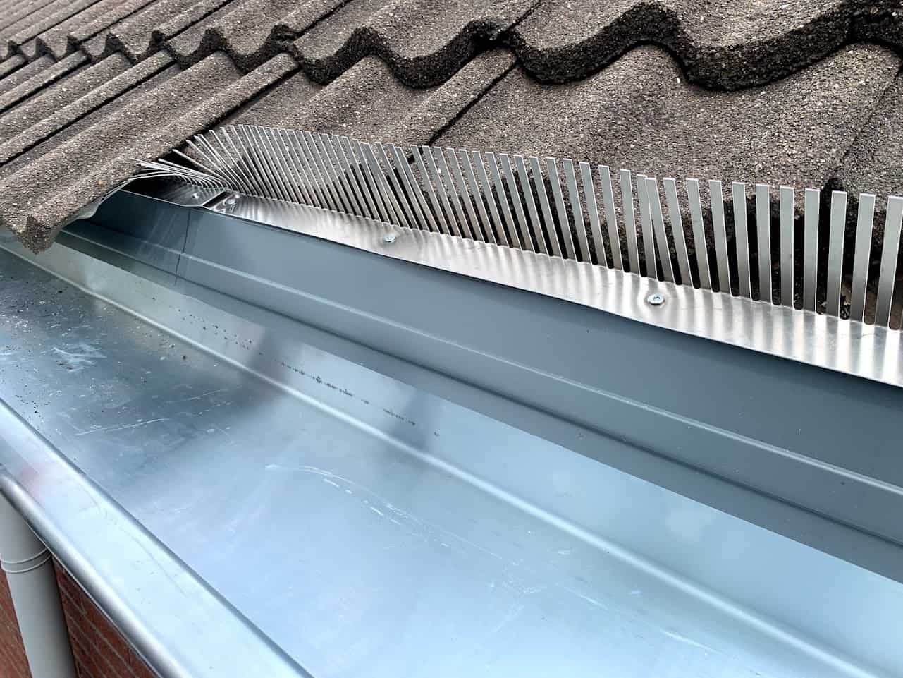 Dakgoot met vogelweringssysteem bestaande uit metalen pinnen op een huis.